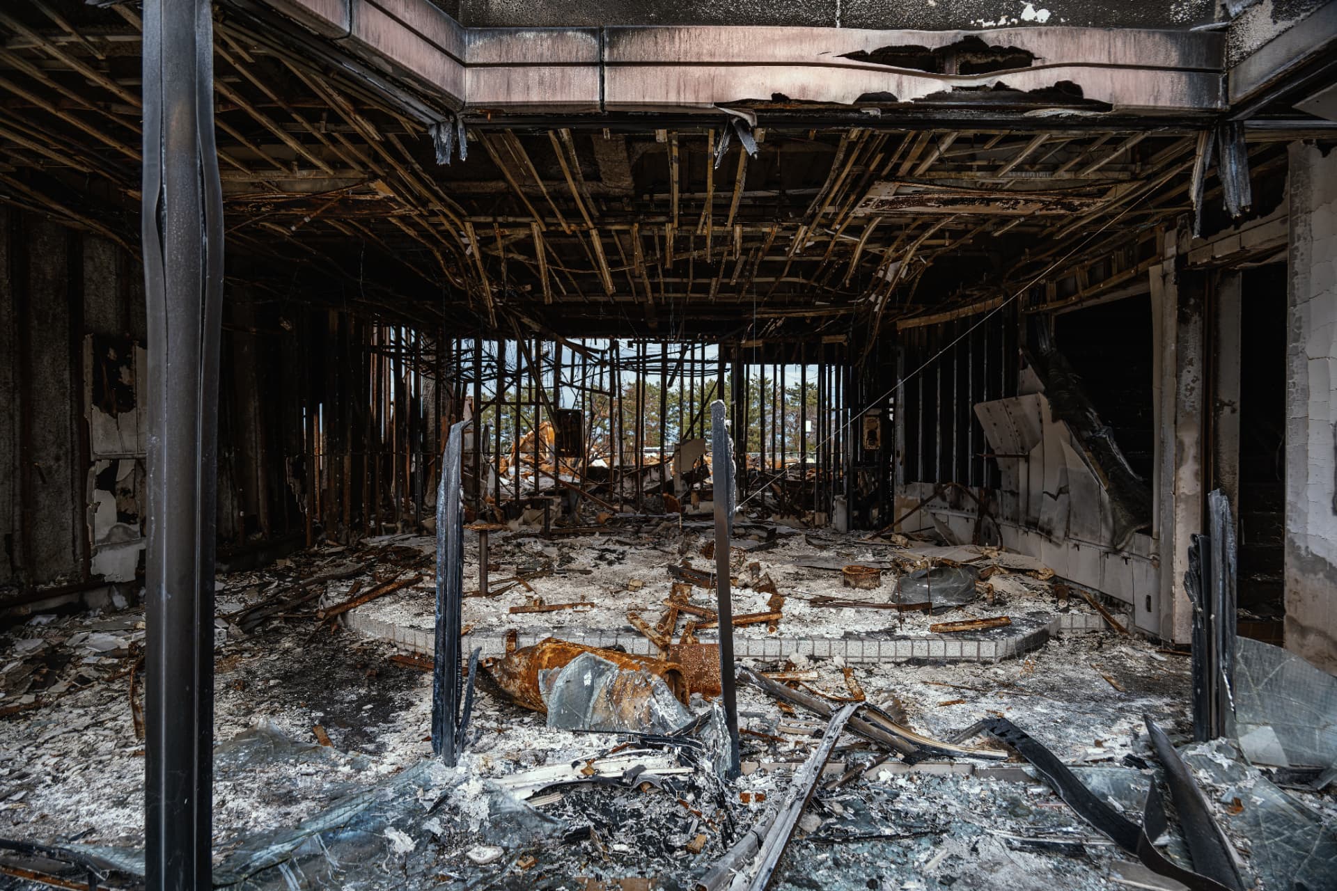 Interior of a fire-damaged building with charred steelwork, collapsed ceiling and debris across the floor