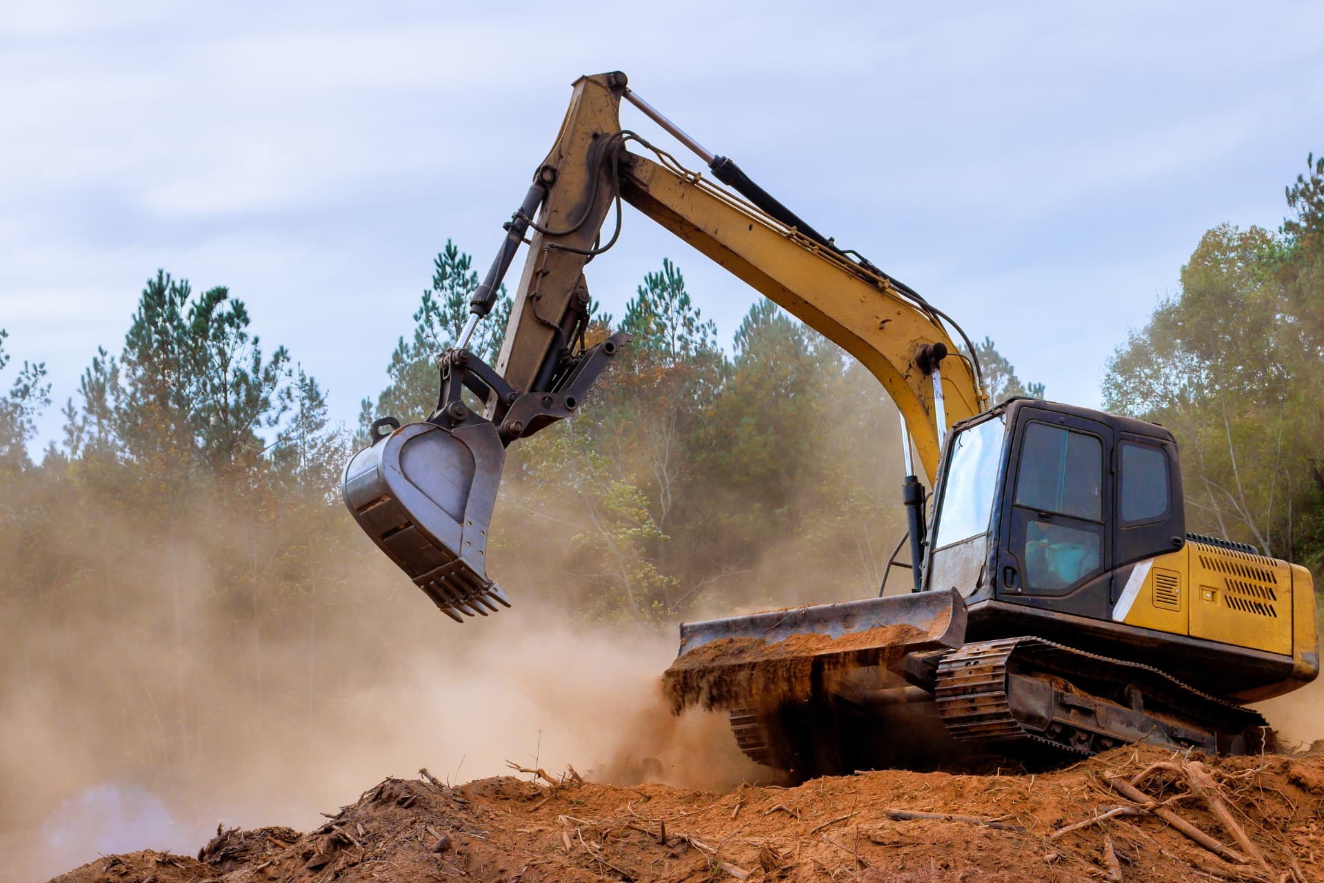 Tracked excavator clearing and levelling ground on a brownfield site in a cloud of dust
