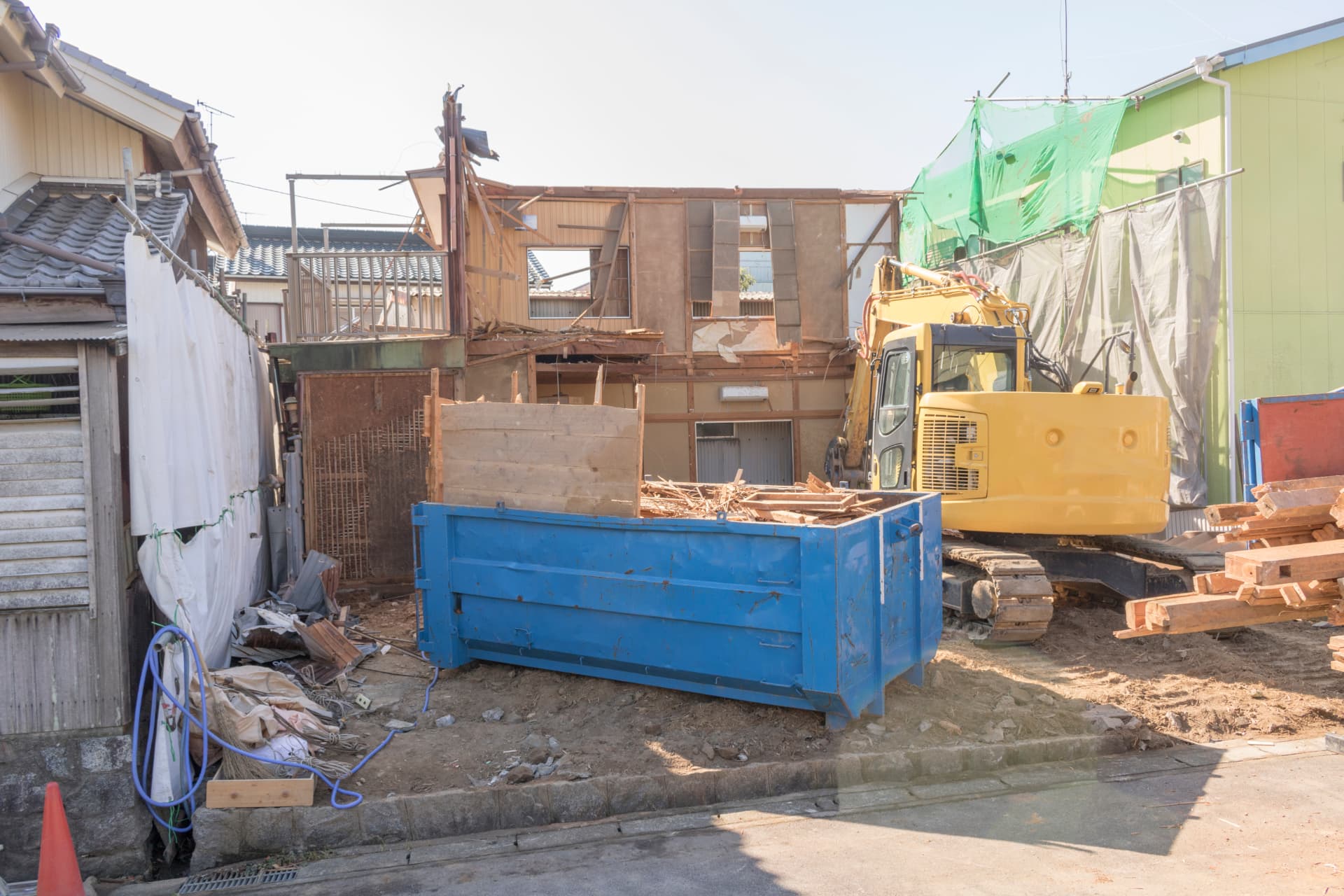 Excavator and waste skip on a tight residential plot part-way through a house demolition