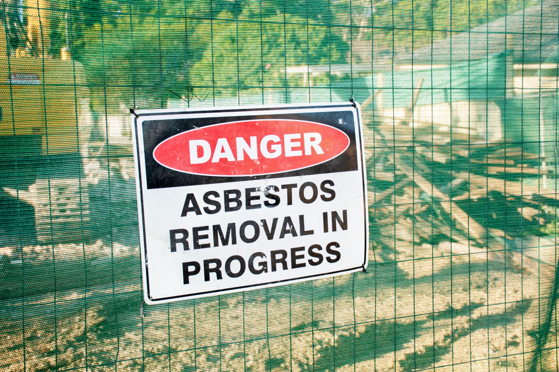 Danger, asbestos removal in progress sign fixed to green site netting around a controlled work area