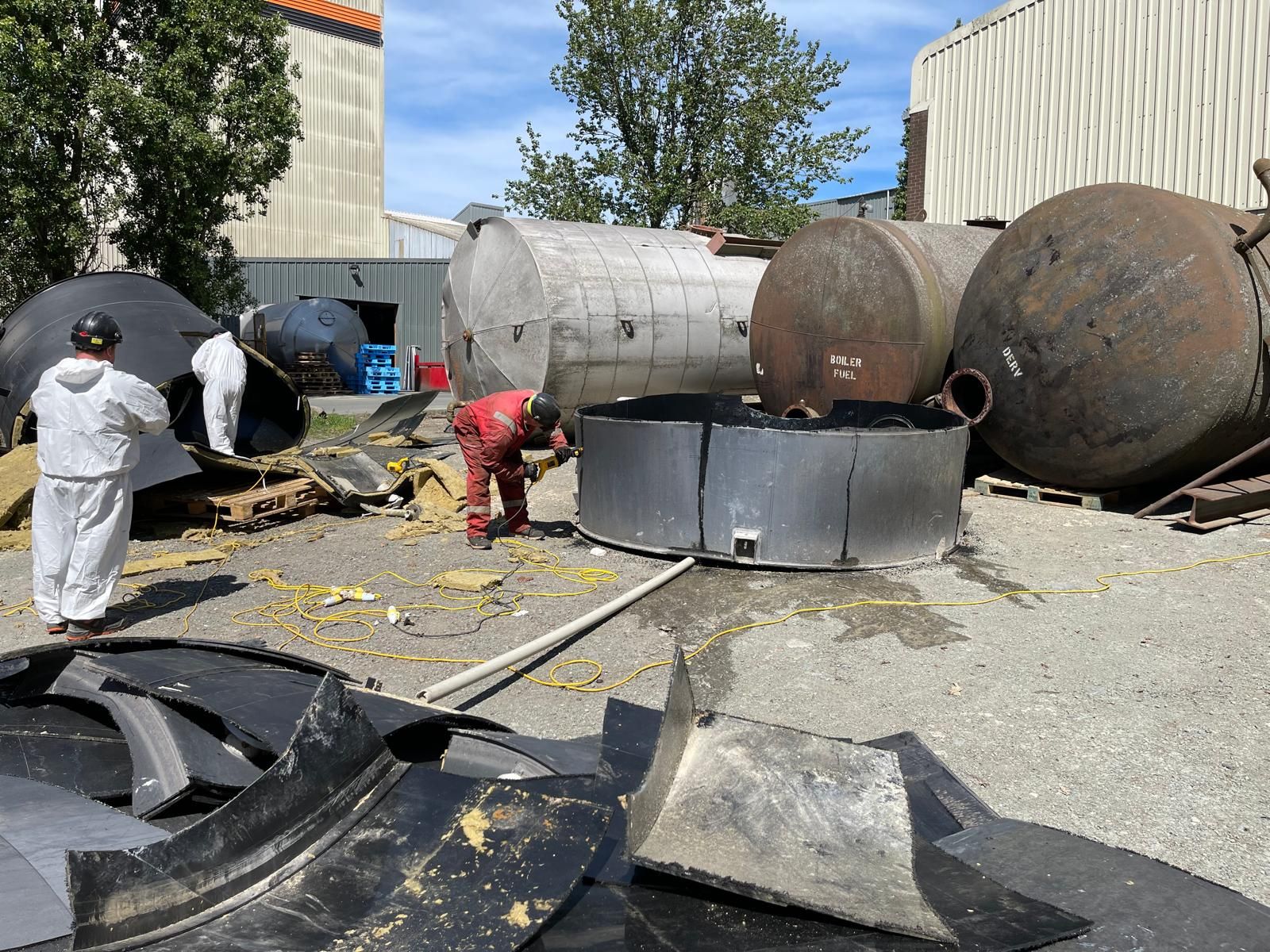 Operatives in protective coveralls cutting up redundant fuel storage tanks during a decommissioning project