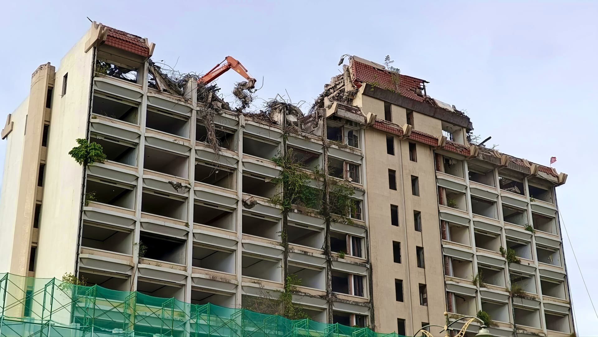 High-reach excavator taking down the upper floors of a large concrete-framed commercial building
